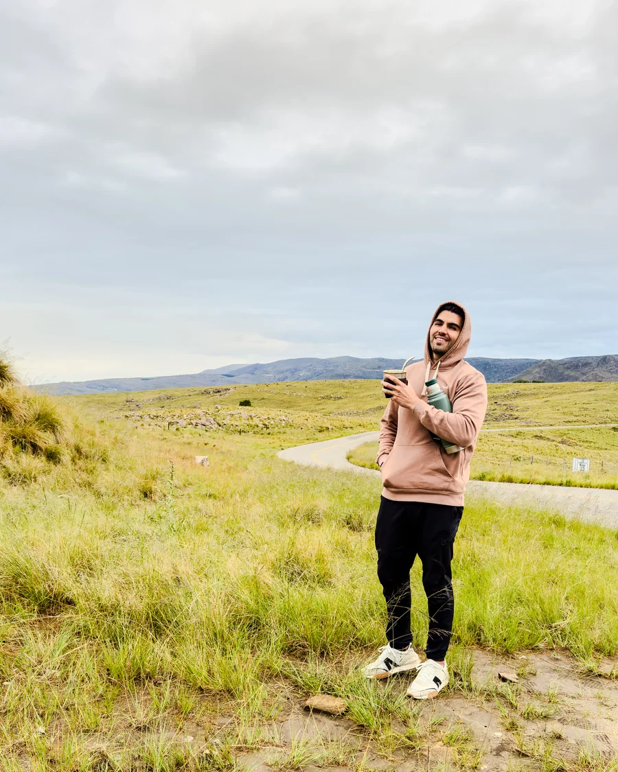 Daniel Arietto sonriendo con un mate en la mano, en un camino de sierras